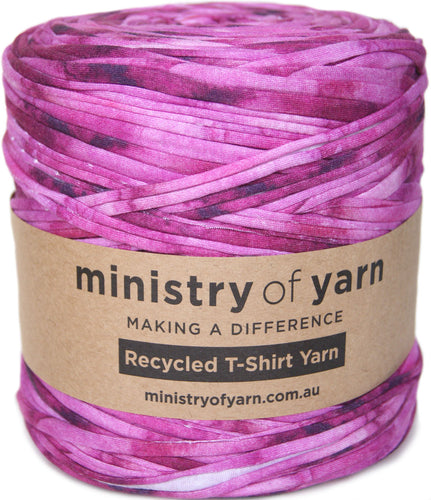 A skein of pink and purple mottled recycled t-shirt yarn wrapped in a brown paper label that reads 'ministry of yarn'.