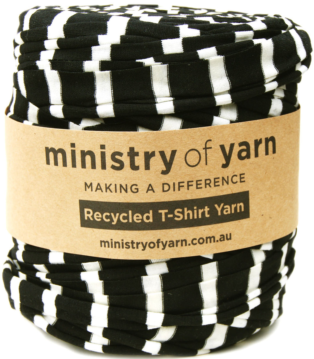 A roll of black and white striped recycled T-shirt yarn wrapped in a brown kraft paper band labeled 'ministry of yarn'.