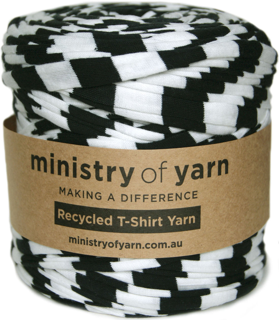 A spool of black and white checkered yarn wrapped in a brown paper label that reads 'ministry of yarn' and 'Recycled T-Shirt Yarn'.