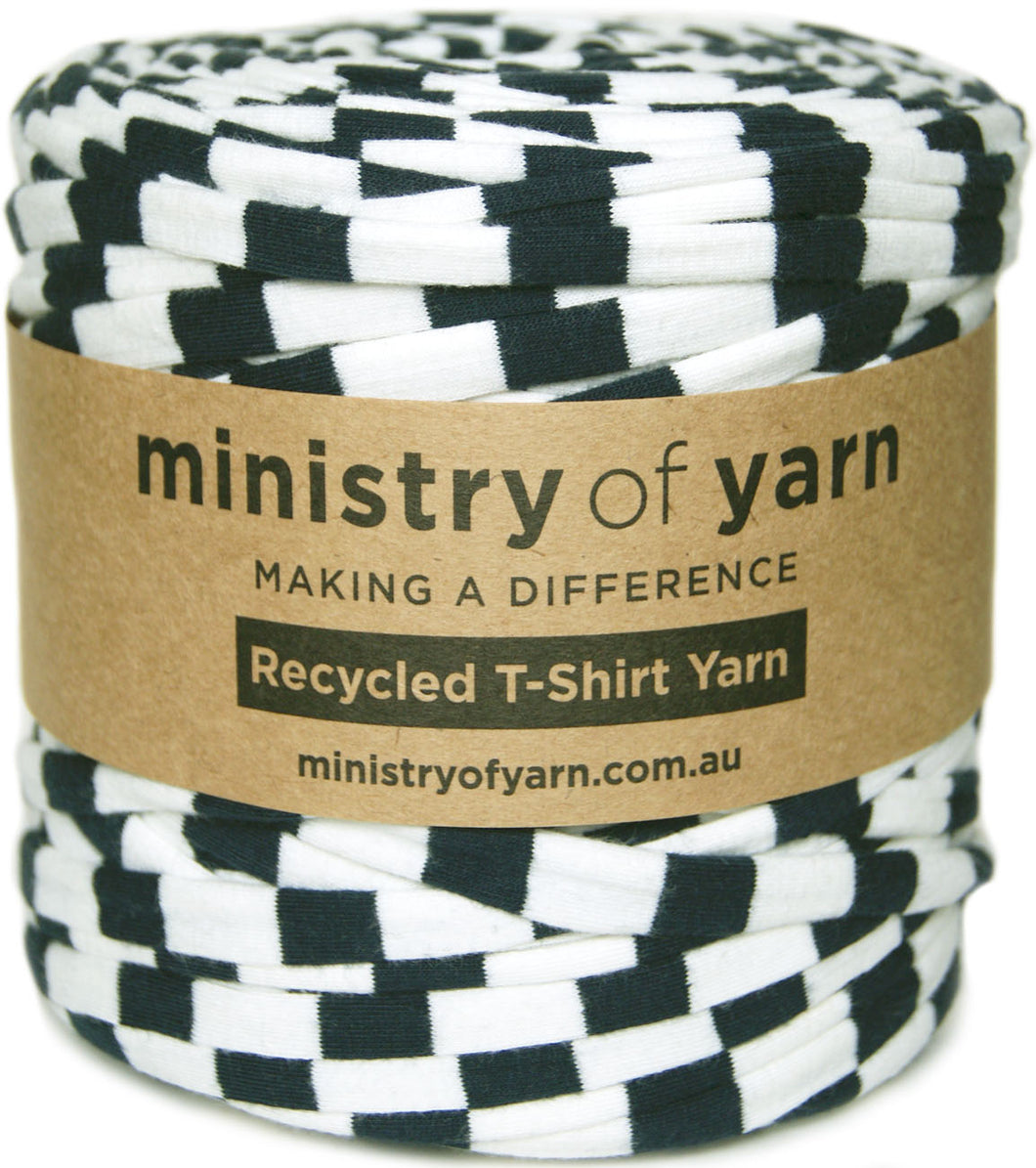 A roll of black and white recycled T-shirt yarn wrapped with a brown kraft paper label that reads 'ministry of yarn'.