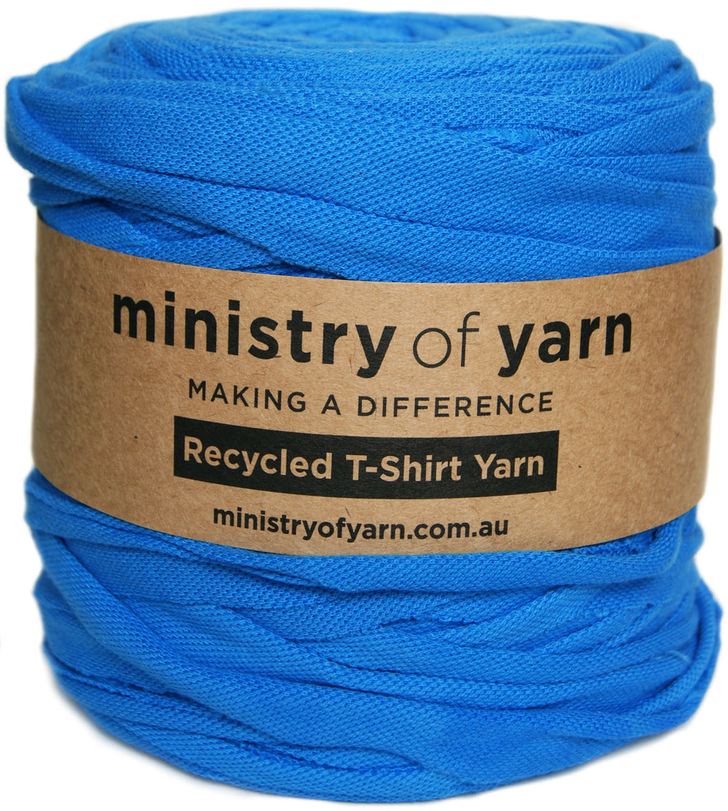 A roll of bright blue recycled t-shirt yarn wrapped with a brown kraft paper label that reads 'ministry of yarn'.