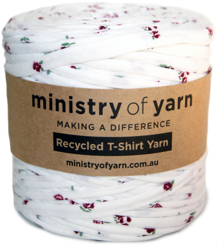 A spool of white recycled T-shirt yarn with a small red and green floral print, wrapped in a brown paper label that reads 'ministry of yarn'.