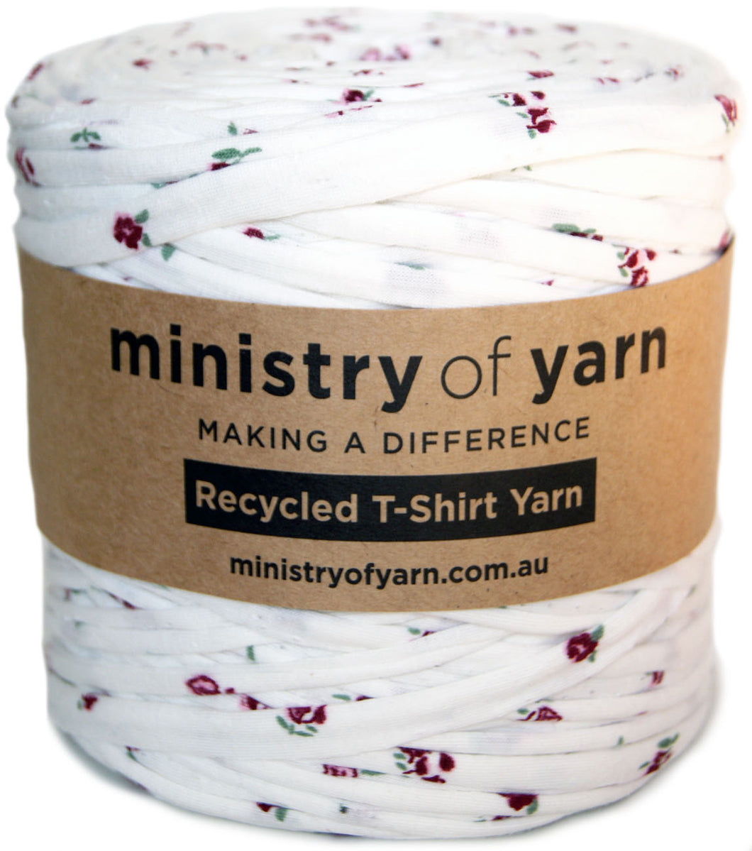 A spool of white recycled T-shirt yarn with a small red and green floral print, wrapped in a brown paper label that reads 'ministry of yarn'.