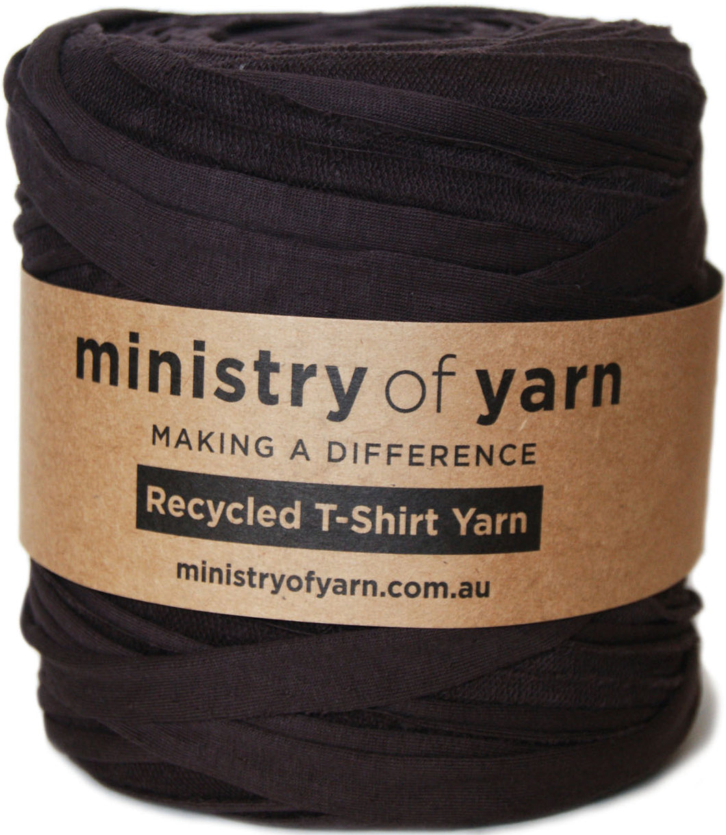 A skein of dark charcoal brown recycled T-shirt yarn wrapped in a brown kraft paper label that reads 'ministry of yarn'.