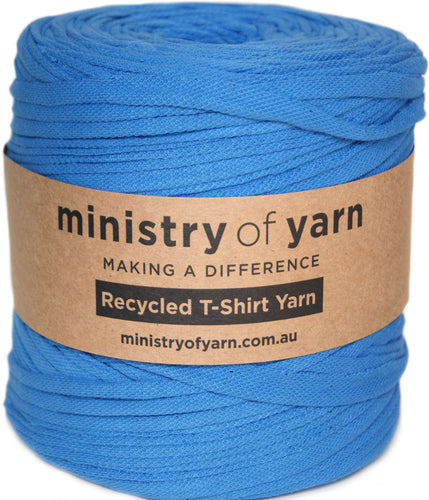 A spool of bright blue recycled T-shirt yarn wrapped with a brown kraft paper label that reads 'ministry of yarn'.