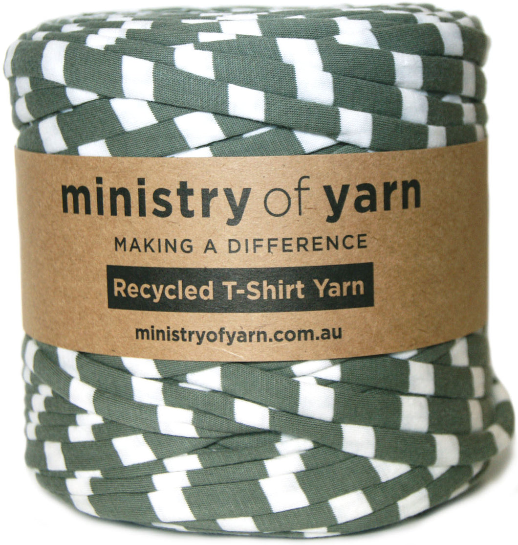 A spool of Ministry of Yarn recycled T-shirt yarn with a green and white woven pattern, wrapped in a brown kraft paper label.