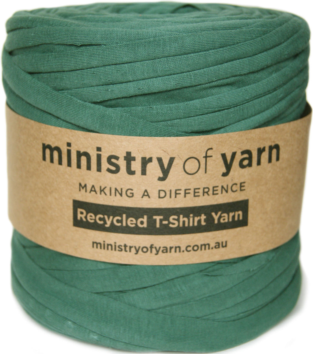 A spool of teal green recycled T-shirt yarn wrapped with a brown kraft paper label that reads 'ministry of yarn'.