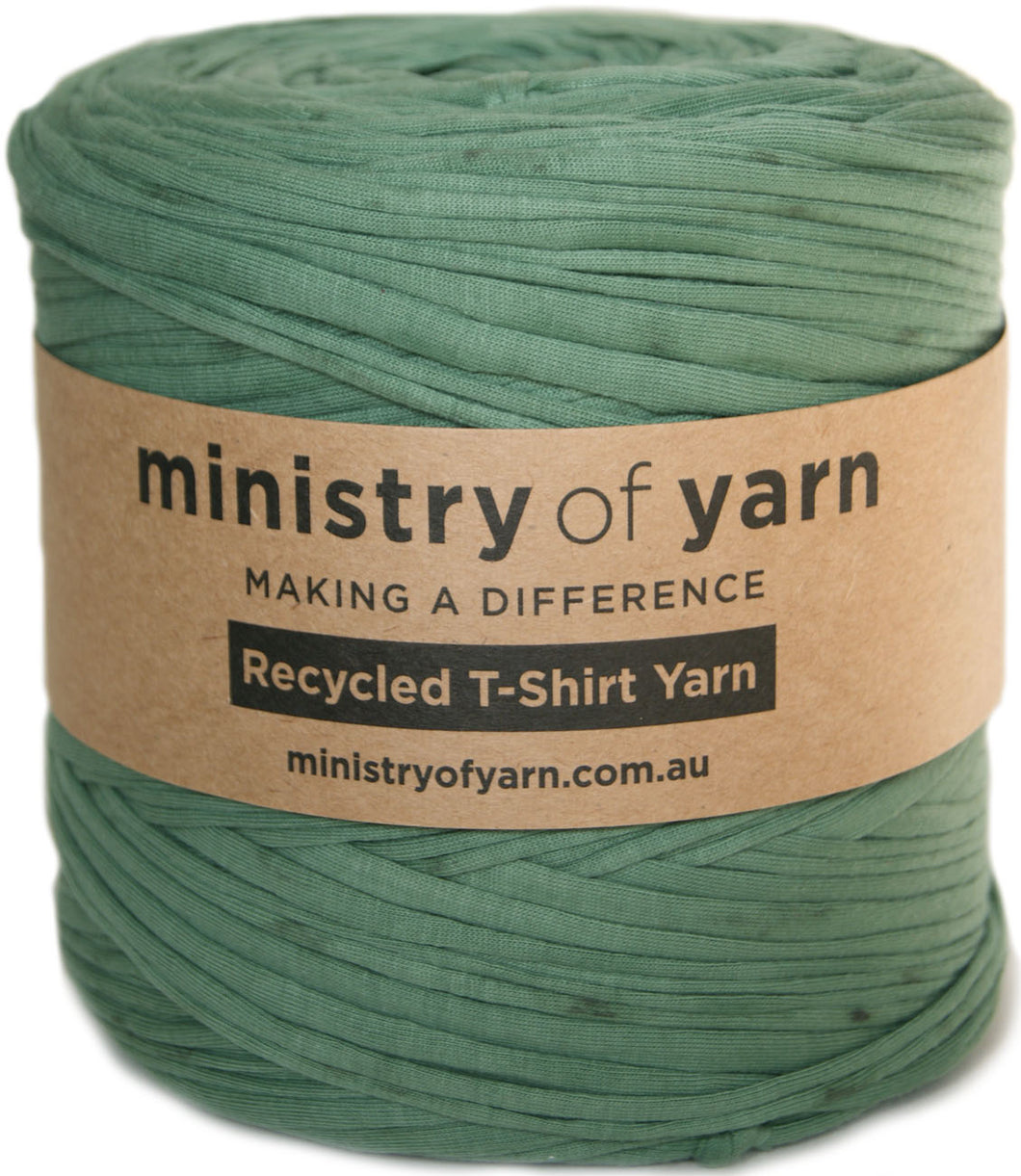 A spool of sage green recycled T-shirt yarn wrapped with a brown paper label that reads 'ministry of yarn' and 'Recycled T-Shirt Yarn'.