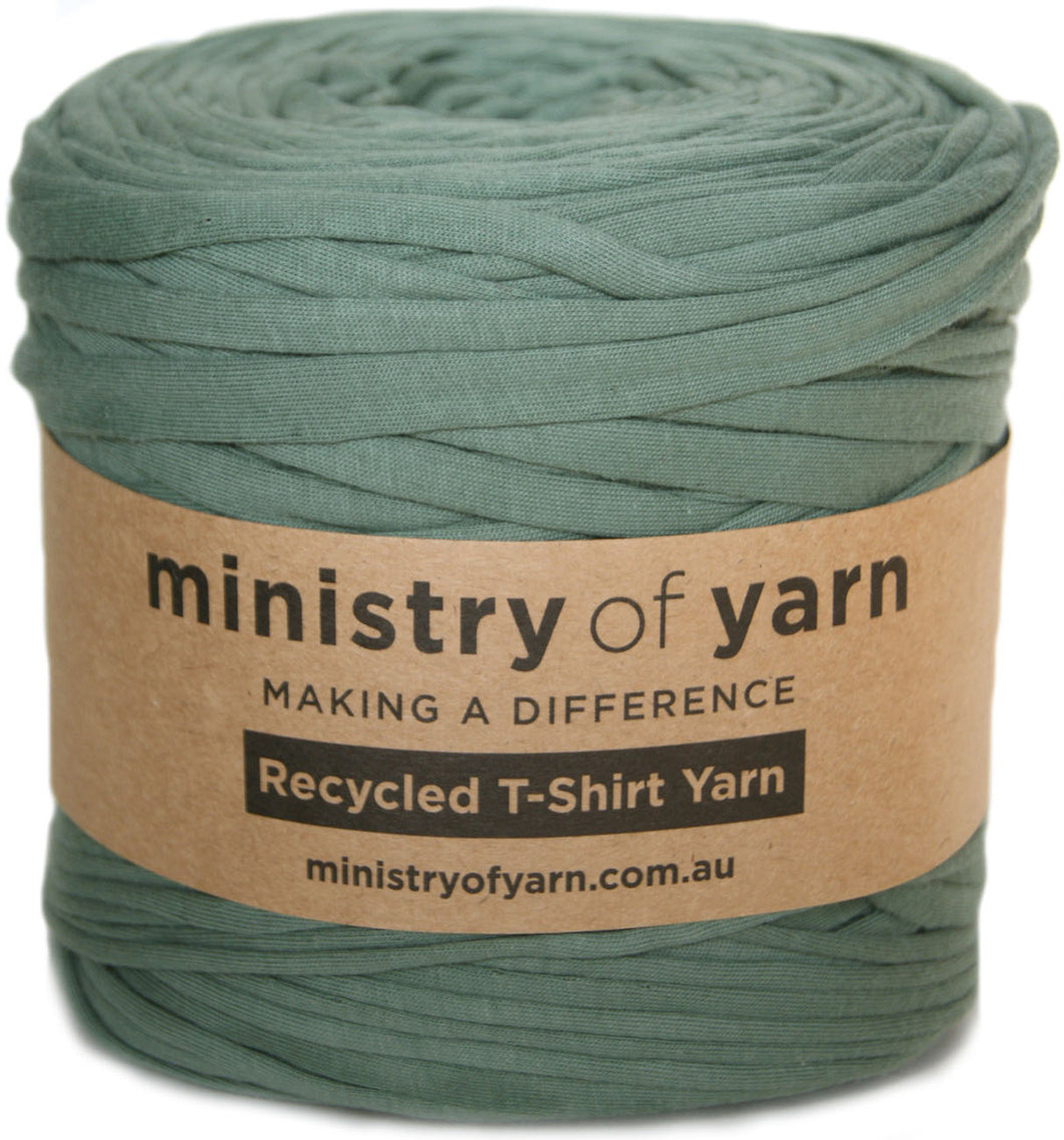 A roll of sage green recycled T-shirt yarn with a brown paper label that reads 'ministry of yarn' and 'Recycled T-Shirt Yarn'.