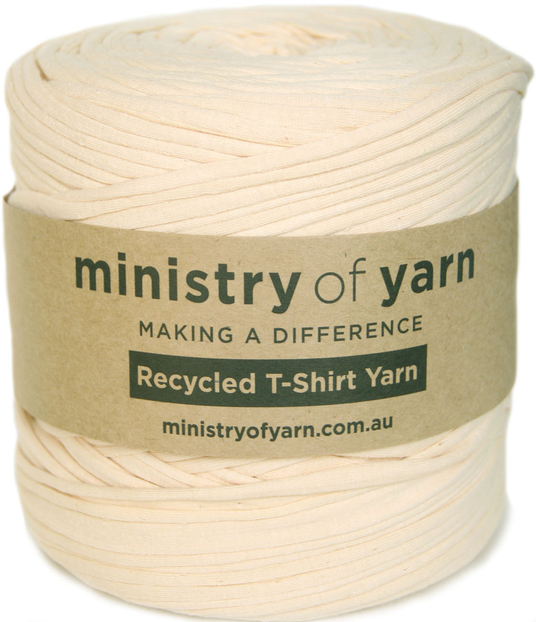 A spool of cream-colored recycled T-shirt yarn wrapped with a brown kraft paper label that reads 'ministry of yarn'.