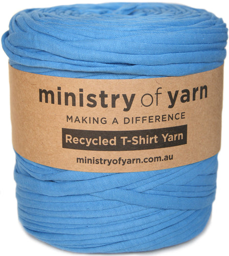 A large spool of sky blue recycled T-shirt yarn wrapped with a brown kraft paper label that reads 'ministry of yarn'.