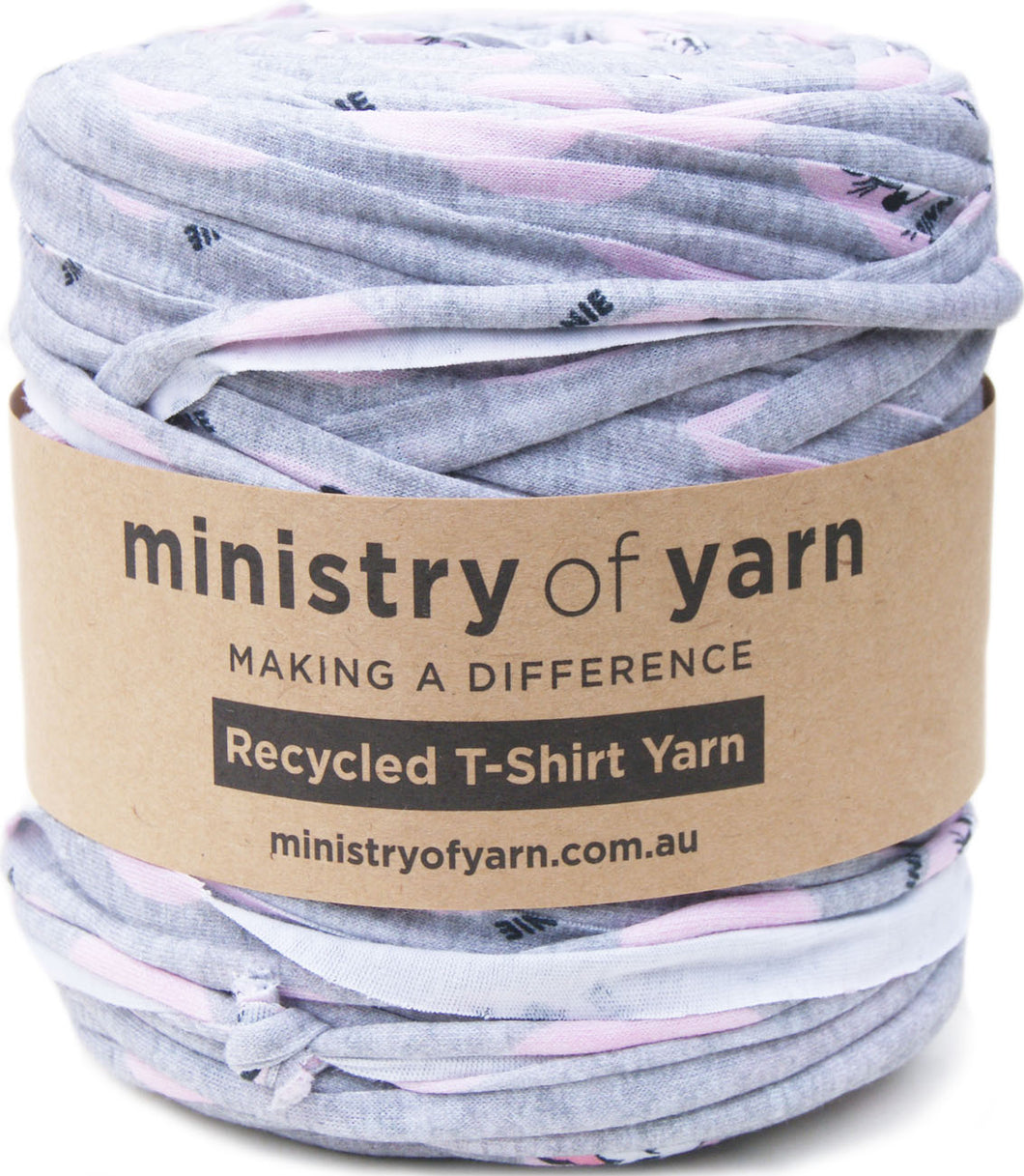 A ball of Ministry of Yarn recycled T-shirt yarn wrapped in a brown paper label, featuring a heather gray base with light pink and Minnie Mouse printed fabric.