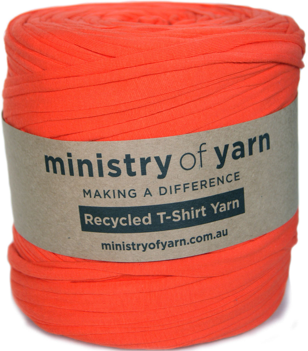 A bright orange-red roll of yarn with a paper label reading 'ministry of yarn' and 'Recycled T-Shirt Yarn' on a white background.
