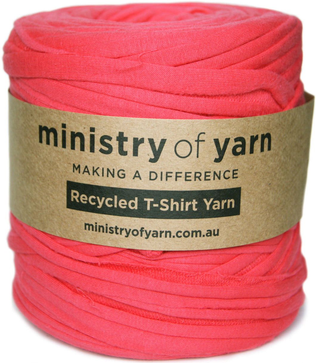 A skein of bright coral pink recycled T-shirt yarn wrapped in a brown kraft paper label that reads 'ministry of yarn'.