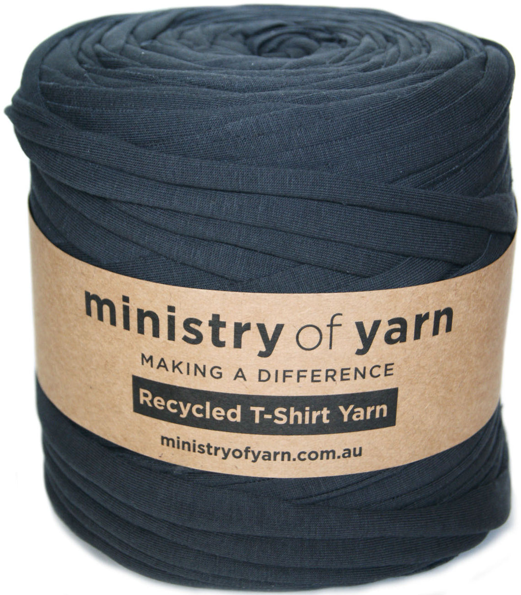 A roll of dark charcoal gray recycled T-shirt yarn wrapped with a brown kraft paper label that reads 'ministry of yarn'.