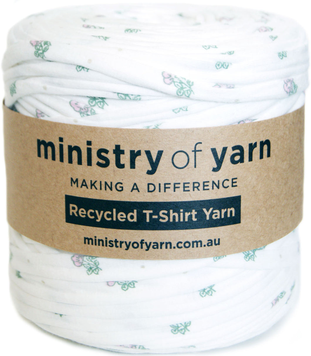 A spool of white recycled T-shirt yarn with a small pastel floral print, wrapped in a brown paper band labeled 'ministry of yarn'.