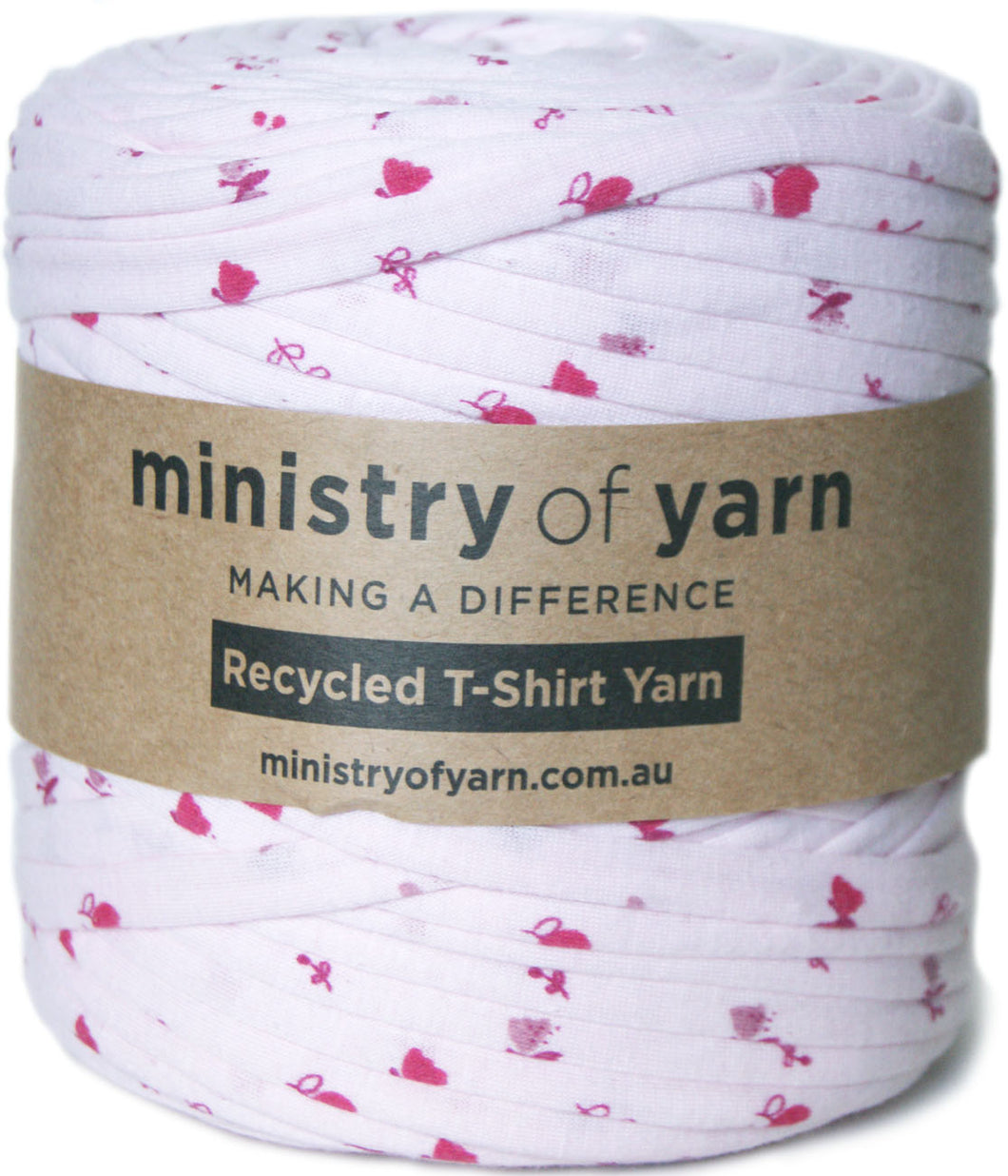 A roll of white recycled T-shirt yarn with a pink heart and bow pattern, wrapped in a brown paper band labeled 'ministry of yarn'.