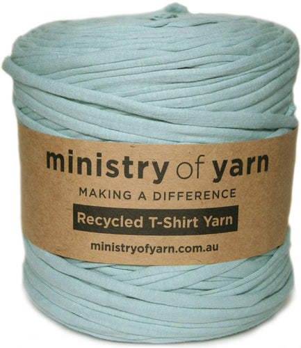 A spool of Ministry of Yarn recycled T-shirt yarn in a dusty light blue-green color, wrapped with a brown kraft paper label.