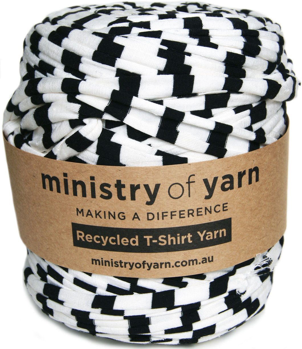 A spool of black and white patterned recycled T-shirt yarn wrapped in a brown paper band labeled 'ministry of yarn'.