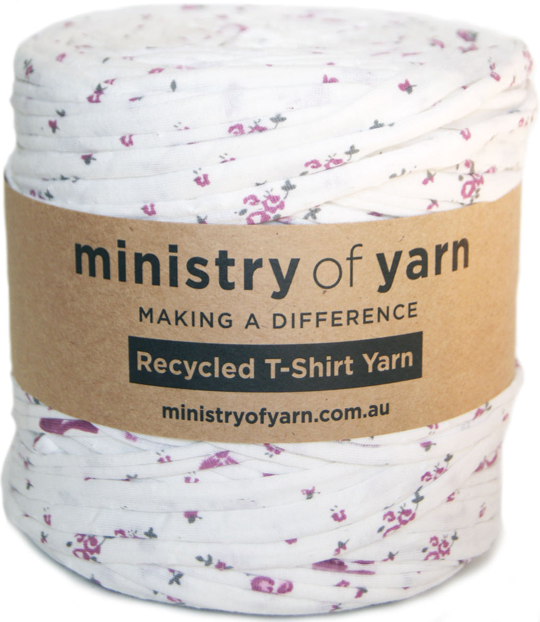 A spool of white recycled T-shirt yarn with a pink and grey floral print, wrapped in a brown paper label that reads 'ministry of yarn'.