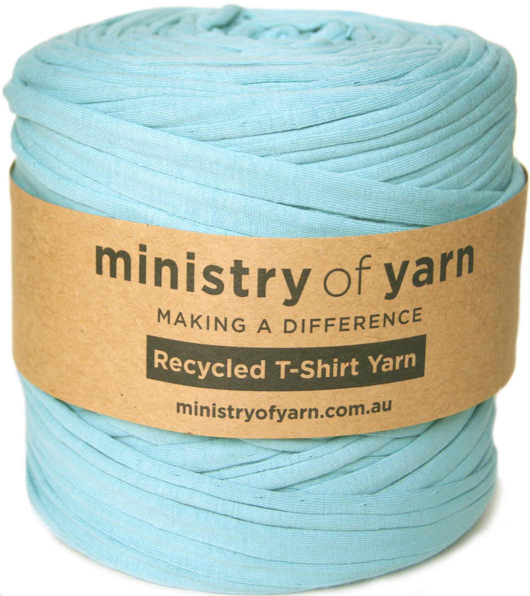 A spool of light blue recycled T-shirt yarn wrapped with a brown paper label that reads 'ministry of yarn'.