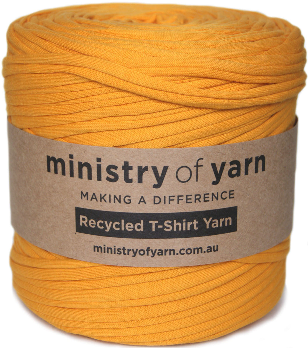 A large spool of mustard yellow recycled T-shirt yarn wrapped with a brown paper label that reads 'ministry of yarn' and 'Recycled T-Shirt Yarn'.