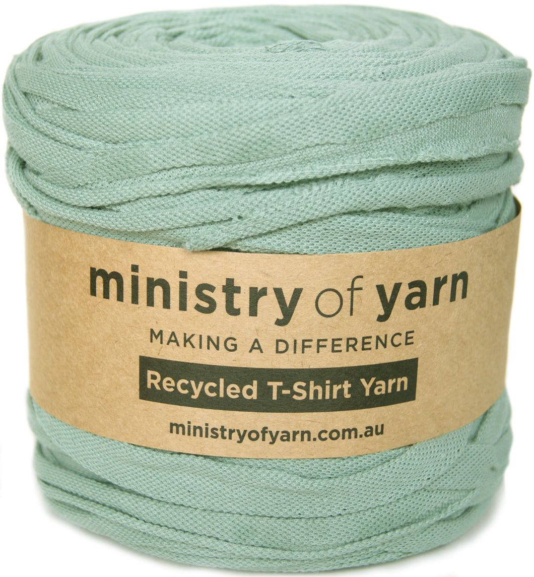 A roll of sage green recycled T-shirt yarn wrapped in a brown kraft paper label that reads 'ministry of yarn'.