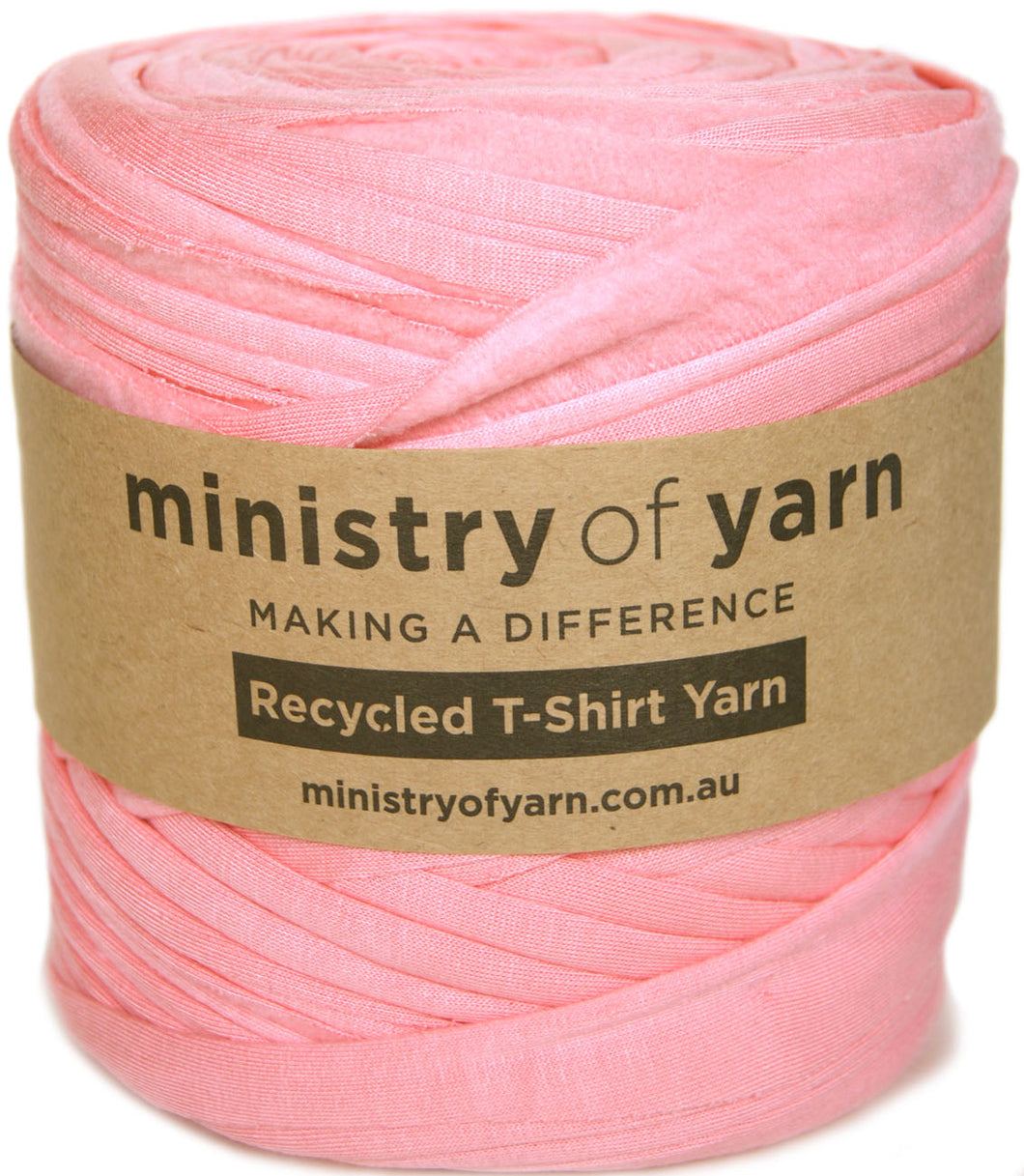 A roll of pink peach recycled T-shirt yarn wrapped in a brown kraft paper band with the brand name 'ministry of yarn' printed on it, set against a plain white background.