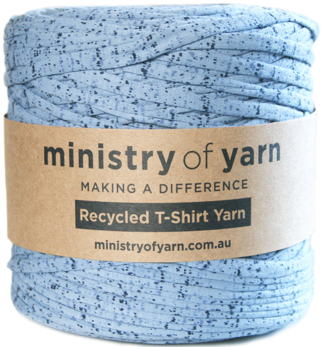 A spool of light blue recycled T-shirt yarn with a brown paper label reading 'ministry of yarn' and 'Recycled T-Shirt Yarn' on a white background.
