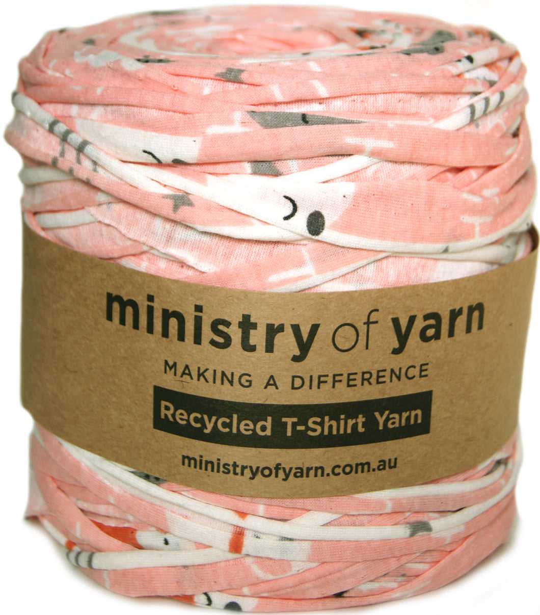 A ball of Ministry of Yarn recycled T-shirt yarn wrapped in a brown paper label, featuring a pink, white, and gray pattern.