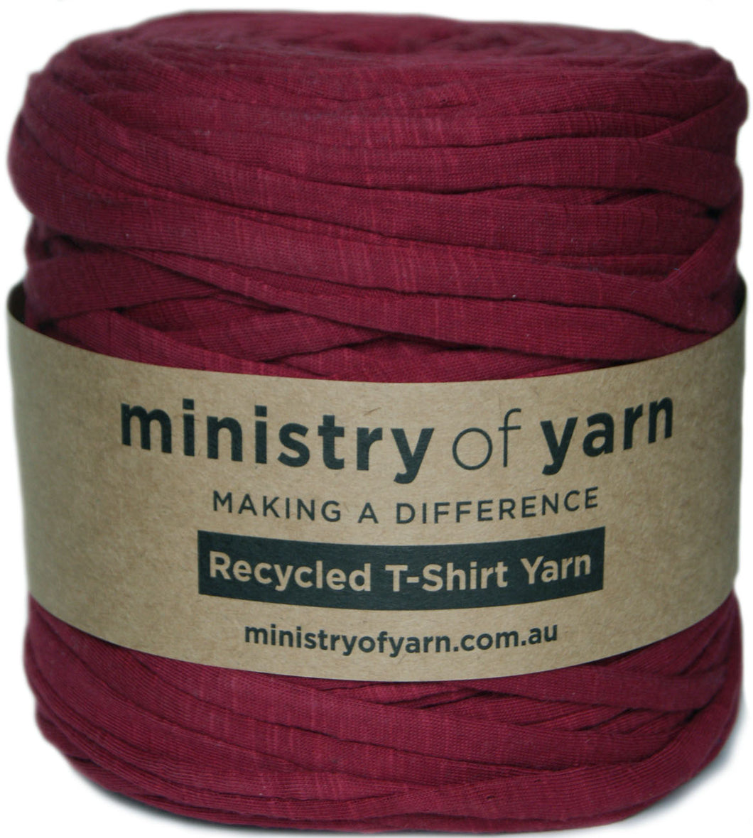 A spool of deep burgundy recycled T-shirt yarn wrapped in a kraft paper label that reads 'ministry of yarn'.